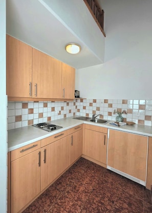Eine Küche mit Holzausstattung, einer weißen Arbeitsplatte, einem Spülbecken und einer gefliesten Rückwand.