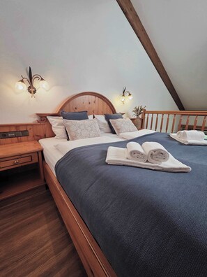 A bedroom with a wooden bed, a nightstand, a wall-mounted light fixture, and a rolled towel on the bed. - Liebevolle Alpen-Maisonette 7 Wörnsmühl (Fischbachau)