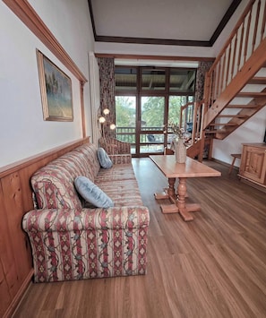 Ein Zimmer mit Holzboden, einem gemusterten Sofa, einem Holztisch und einer Treppe.