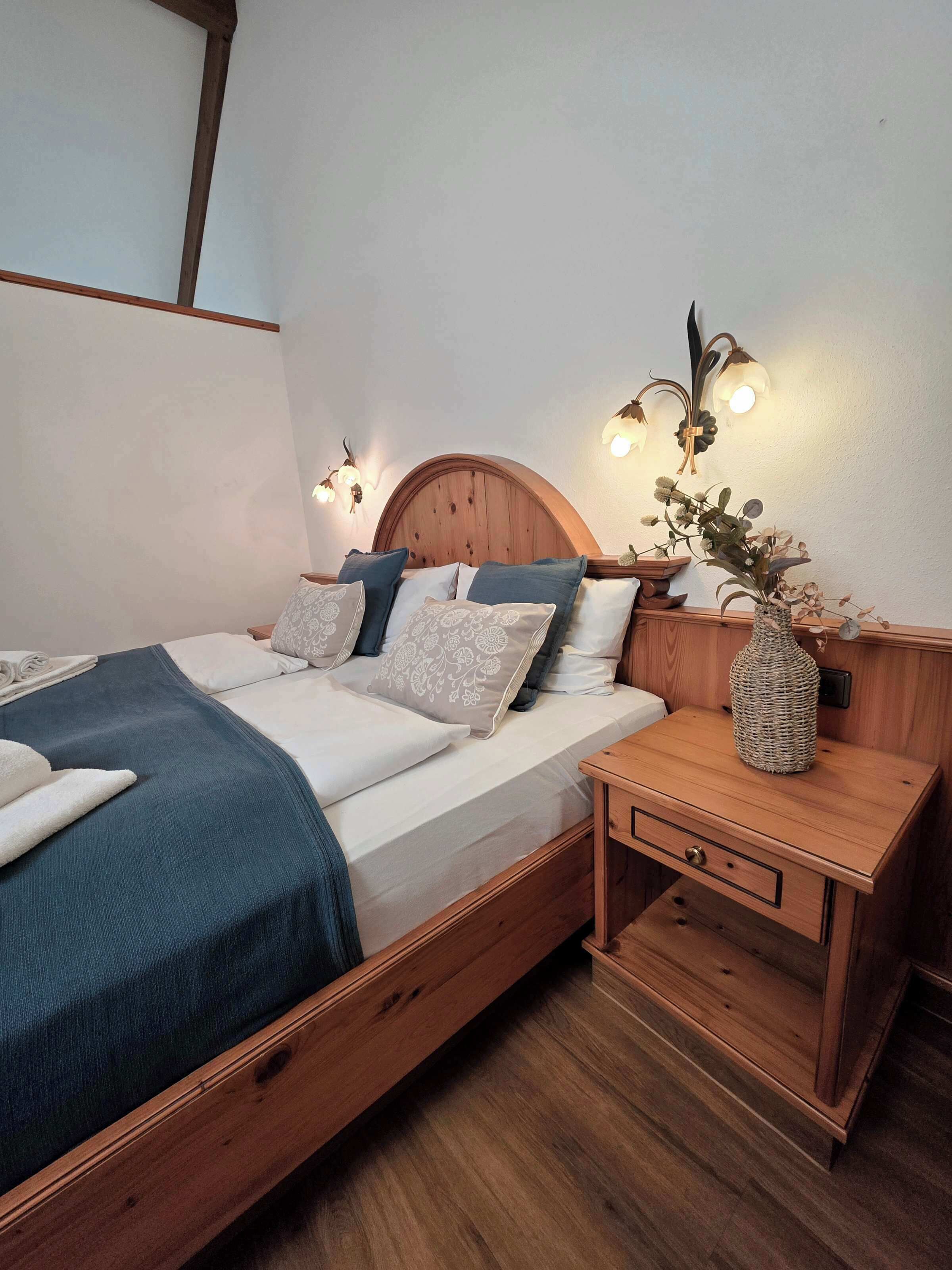 A bedroom with a wooden bed, bedside tables, and wall-mounted lighting.