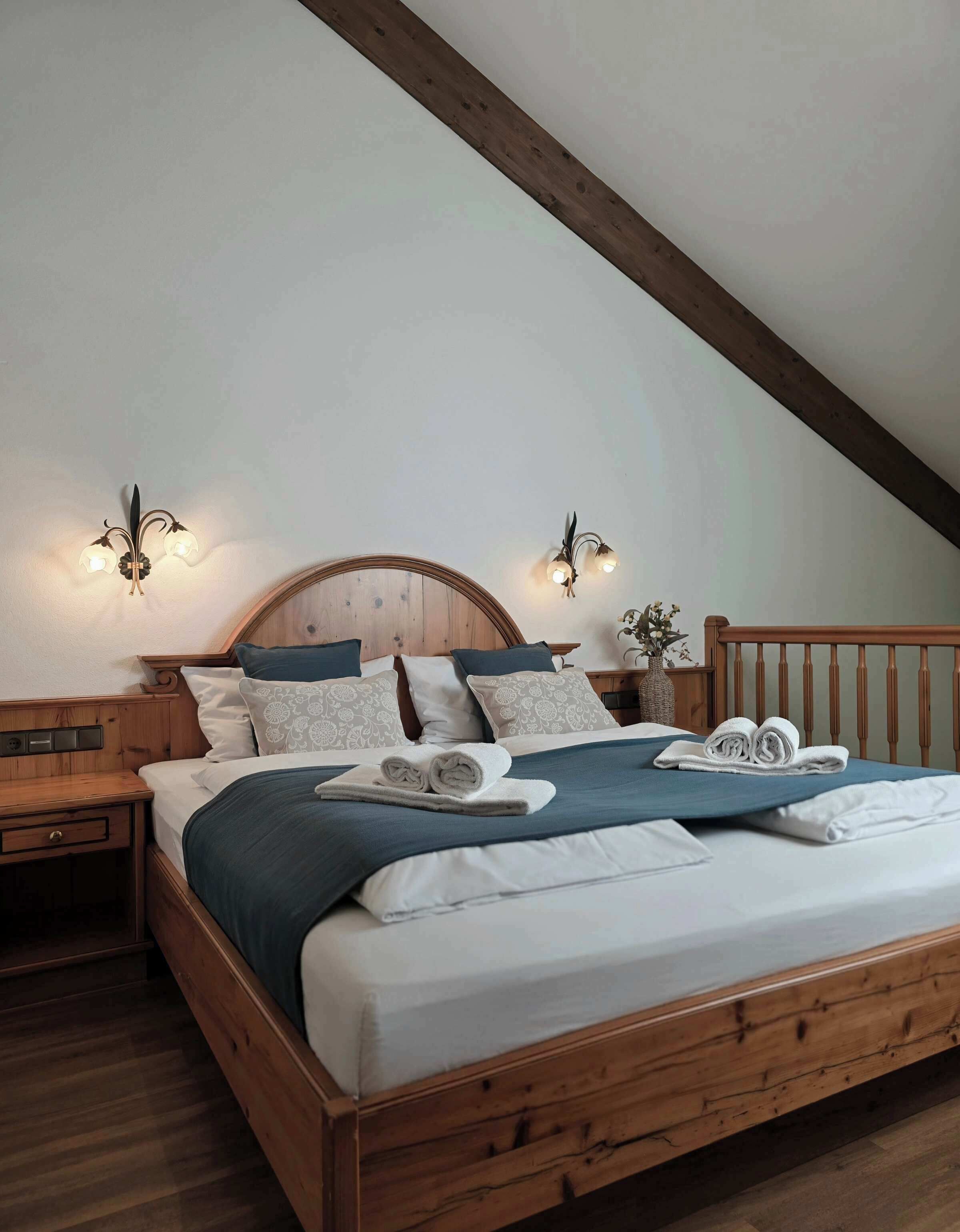 A bedroom with a wooden bed, white bedding, and two wall-mounted light fixtures.