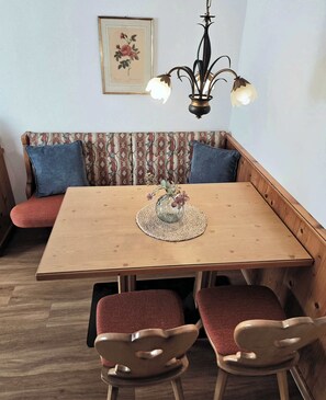 Ruokailutila, jossa on puinen pöytä, punaisilla pehmusteilla varustetut tuolit, kudottu aluslauta ja kukkakoriste.