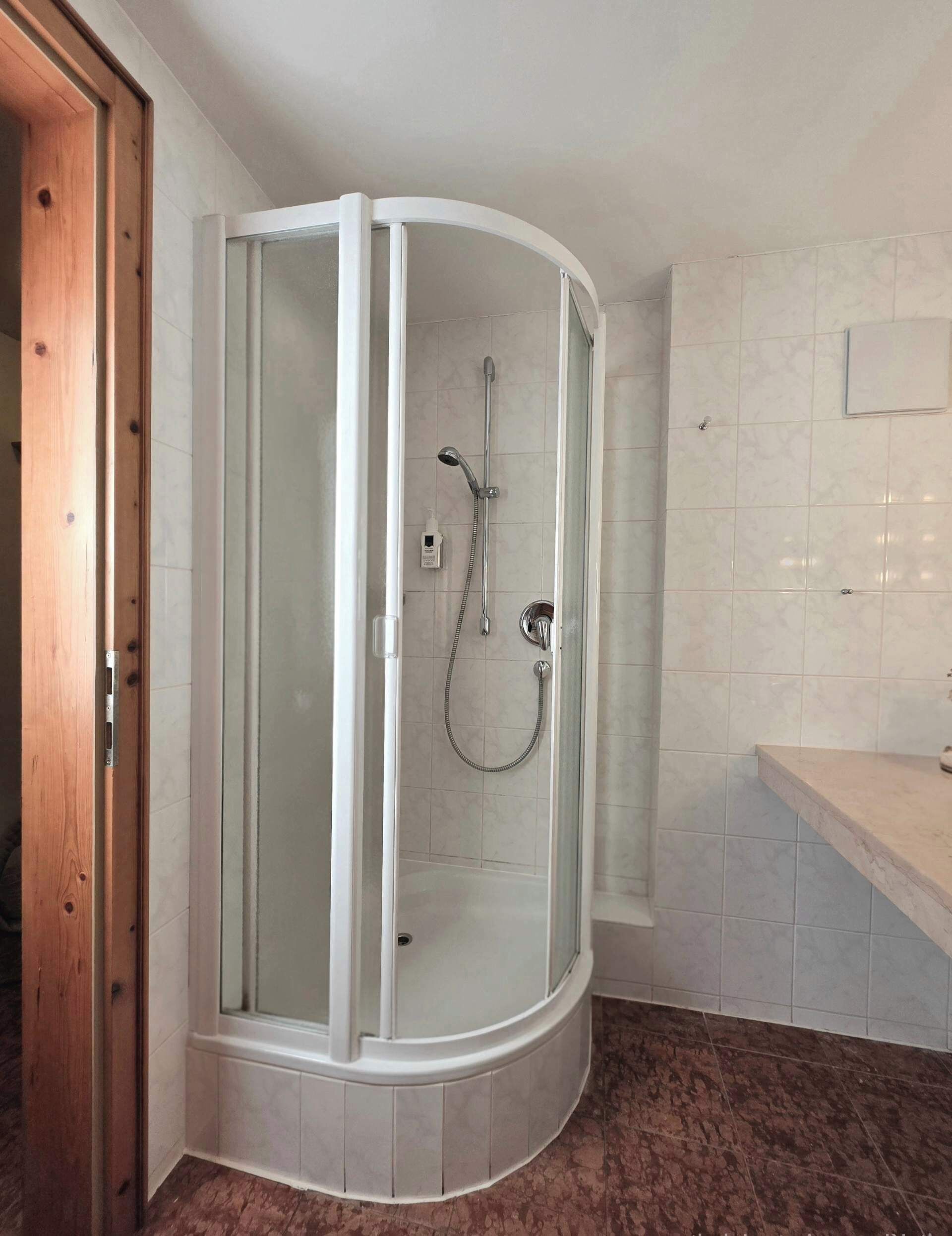 Box de ducha con mampara de vidrio, cabezal de ducha de mano y grifo empotrado.
