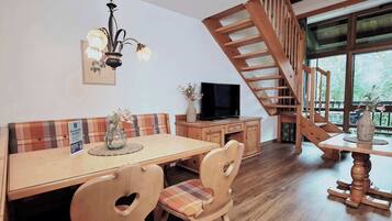 A dining area with a wooden table, chairs, a chandelier, a television, and a staircase.