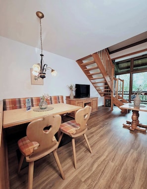 Ein Essbereich mit Holztisch, Stühlen, einer Chandelüstere, einem Fernseher und einer Treppe.