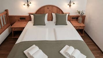 A double bed with two pillows, wooden headboard, nightstands, wall sconces, and a vase with flowers.