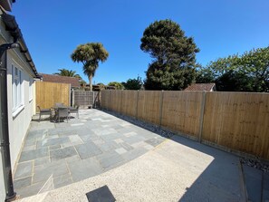 A patio with stone flooring, a wooden fence, and a table with chairs.