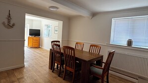 Ein Essbereich mit Holztisch und Stühlen, im Hintergrund eine Küche und ein Fenster mit Jalousien.