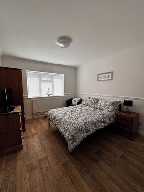 Une chambre Ă coucher comprenant un lit, une commode, une table de chevet, une fenĂȘtre avec des stores, un radiateur et un luminaire au plafond.