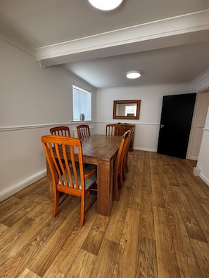 A dining room with a wooden table and chairs, a window with blinds, a mirror on the wall, and a door.