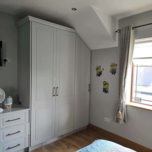 A bedroom with a wardrobe, a bed, a window with curtains, and wall decorations.