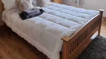 A bed with a wooden frame and white bedding, a small bedside table with a fan, and a window with curtains.