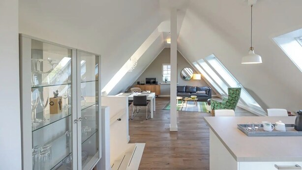 En modern lägenhet i loftstil med matplats, kök och vardagsrum, med takfönster och ett glaskåp.