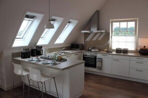 Et moderne køkken med ovenlys, en central ø, hvide skabe og udsigt til grønne omgivelser.