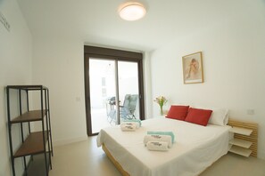 Habitació d'hotel amb un llit, escriptori, cadira, prestatge i una porta corredissa de vidre a l'exterior.