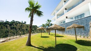Um hotel moderno com área de piscina, palmeiras e guarda-sóis de palha.