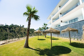 Ein modernes Hotel mit Poolanlage, Palmen und reetgedeckten Sonnenschirmen.