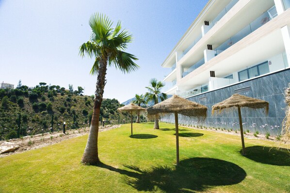 Un hotel modern amb zona de piscina, palmeres i ombrelles de canyes.