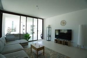 Ein Wohnzimmer mit einer Couch, einem Couchtisch, einem Fernseher und einem großen Fenster mit Blick auf Gebäude.