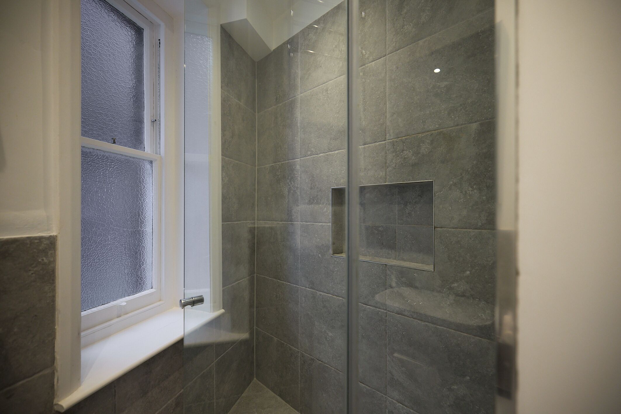 Een douche met glazen deuren, een raam en een betegelde wand.
