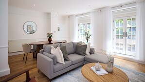 A modern living room with a grey sectional sofa, a round wooden coffee table, and a dining area with a round table and chairs. - Sage & Ivory - Maida Vale (London)