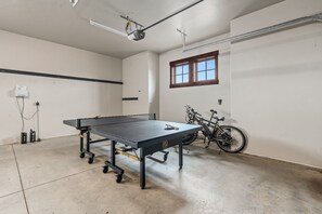 Et bordtennisbord i et rum med en cykel, et vindue og en projektor monteret i loftet.
