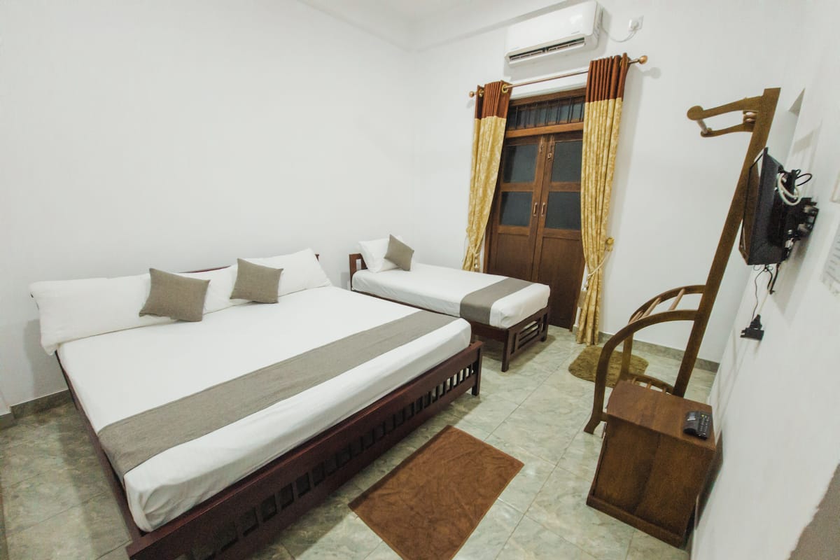 A bedroom with two beds, a wooden chair, a brown rug, and a wooden wardrobe.