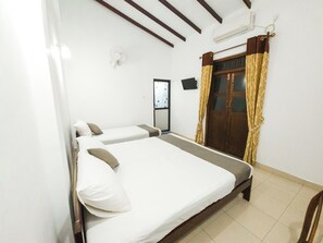 A room with two single beds, a wall-mounted air conditioner, a small table, and a window with curtains. - Nilaro Holiday Resort (Anuradhapura)