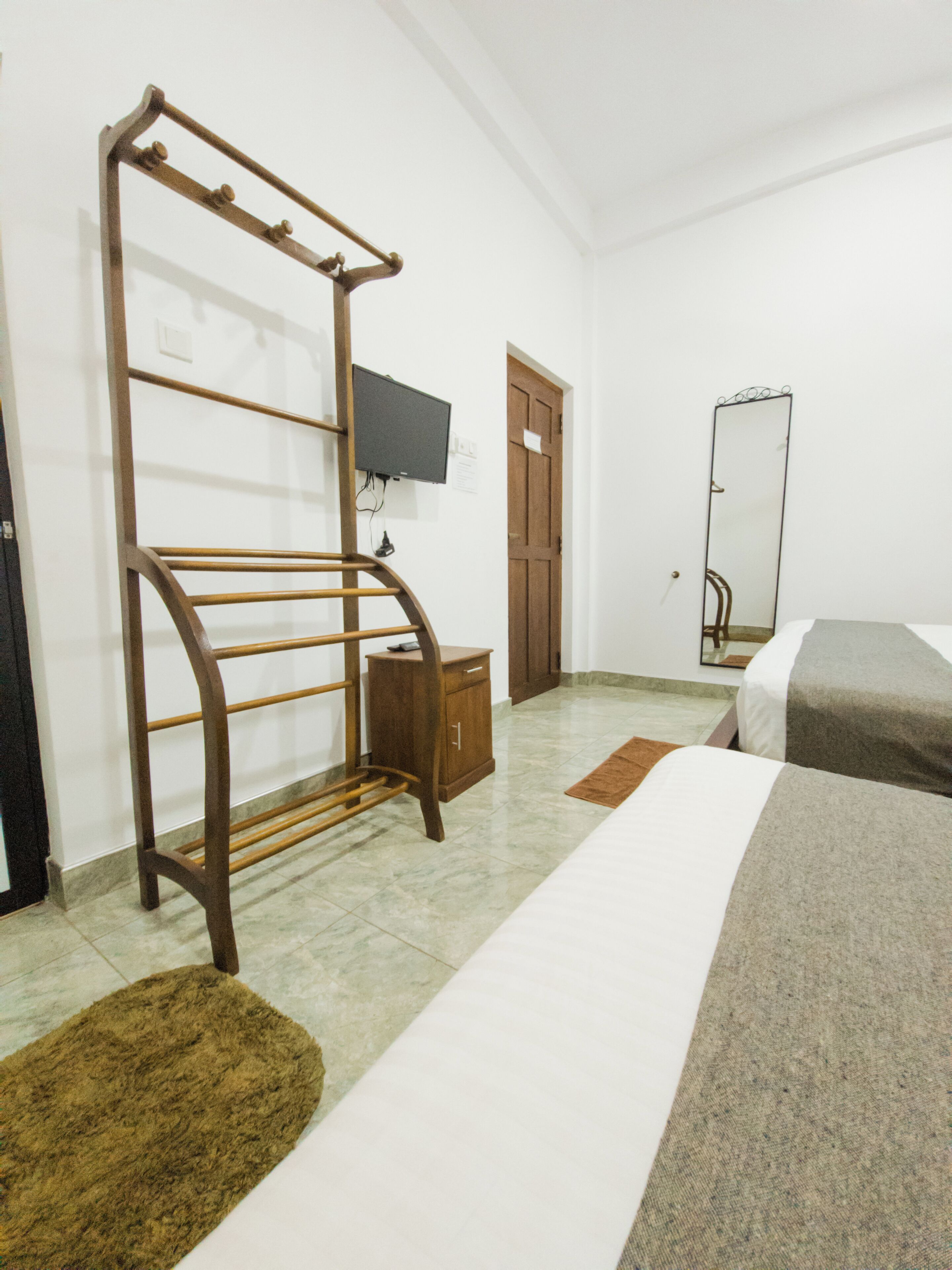 A bedroom with a bed, a wooden wardrobe, a television mounted on the wall, and a mirror.