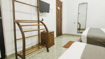 A bedroom with a bed, a wooden wardrobe, a television mounted on the wall, and a mirror.