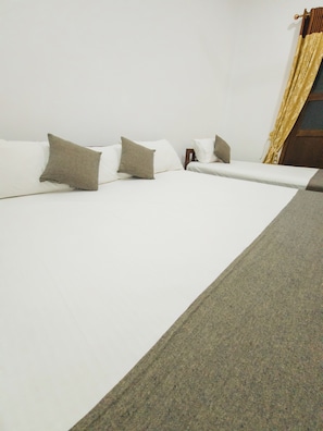 A single bed with white bedding and a grey throw, a wooden nightstand, and a window with curtains.