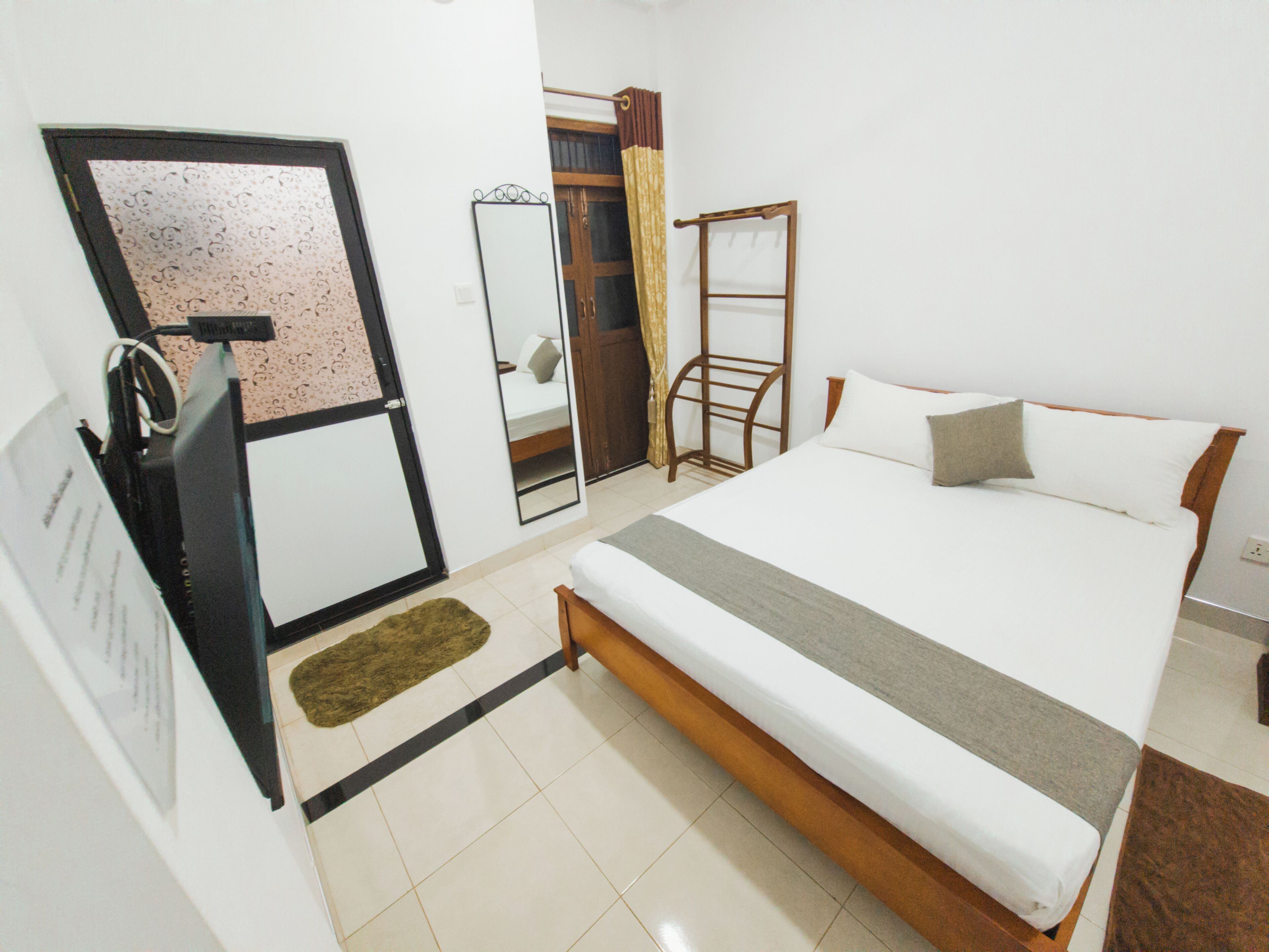 A bedroom with a bed, a wooden chair, a mirror, and a door.
