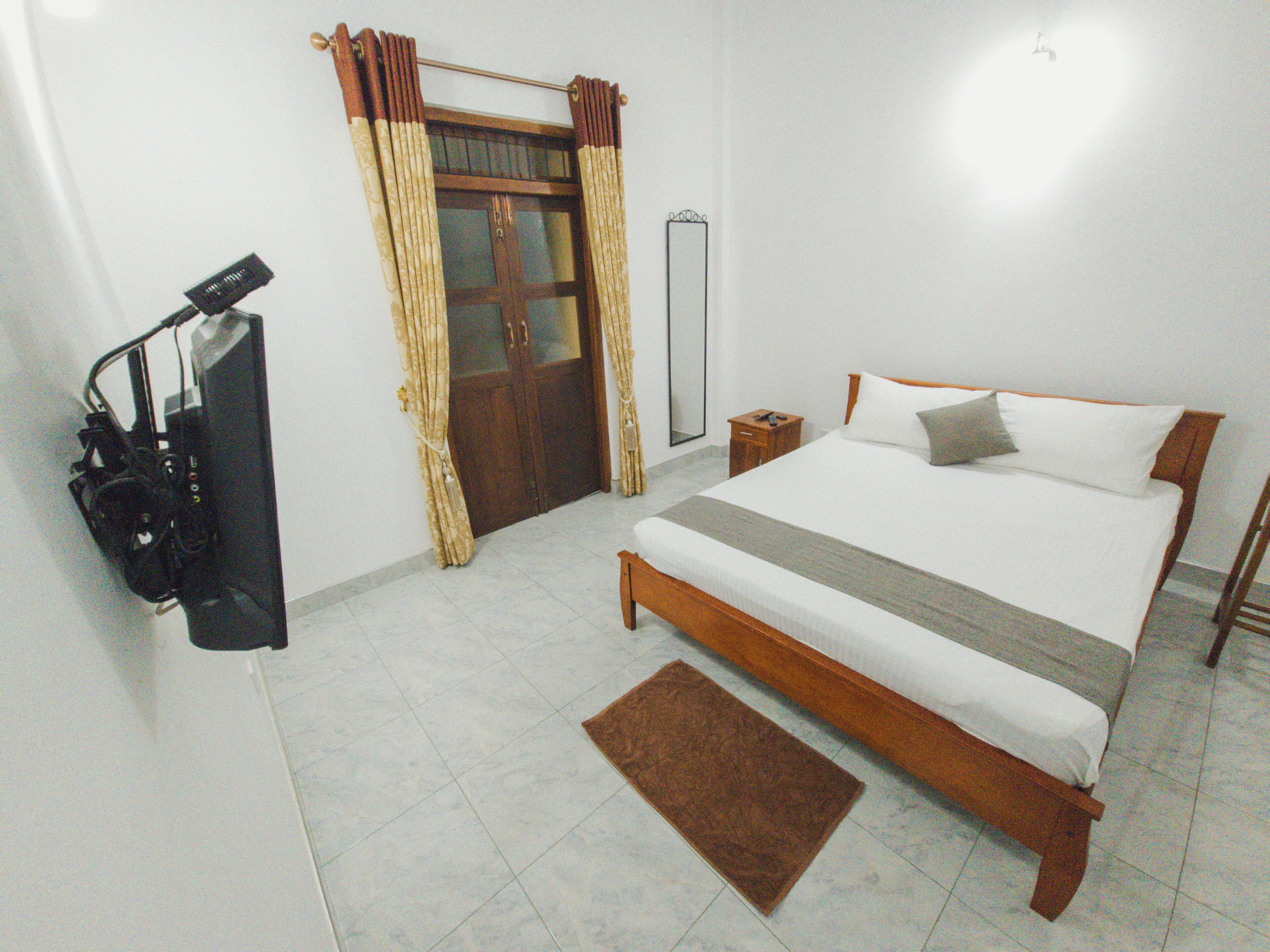 A bedroom with a bed, a wooden nightstand, a mirror, a door with curtains, and a small rug.