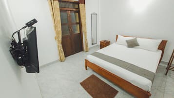 A bedroom with a bed, a wooden nightstand, a mirror, a door with curtains, and a small rug.