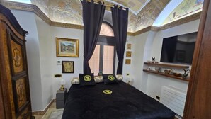 Un dormitorio con una cama grande, televisión, escritorio y techo decorativo.