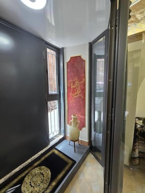 A hallway with a dark wall, a red decorative panel, a vase, and a patterned rug. - THE ETRURIAN RAPSODY (Roma)