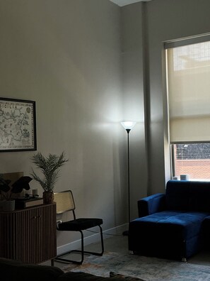 A room with a blue sofa, a standing lamp, a framed map, a potted plant, and a radiator.