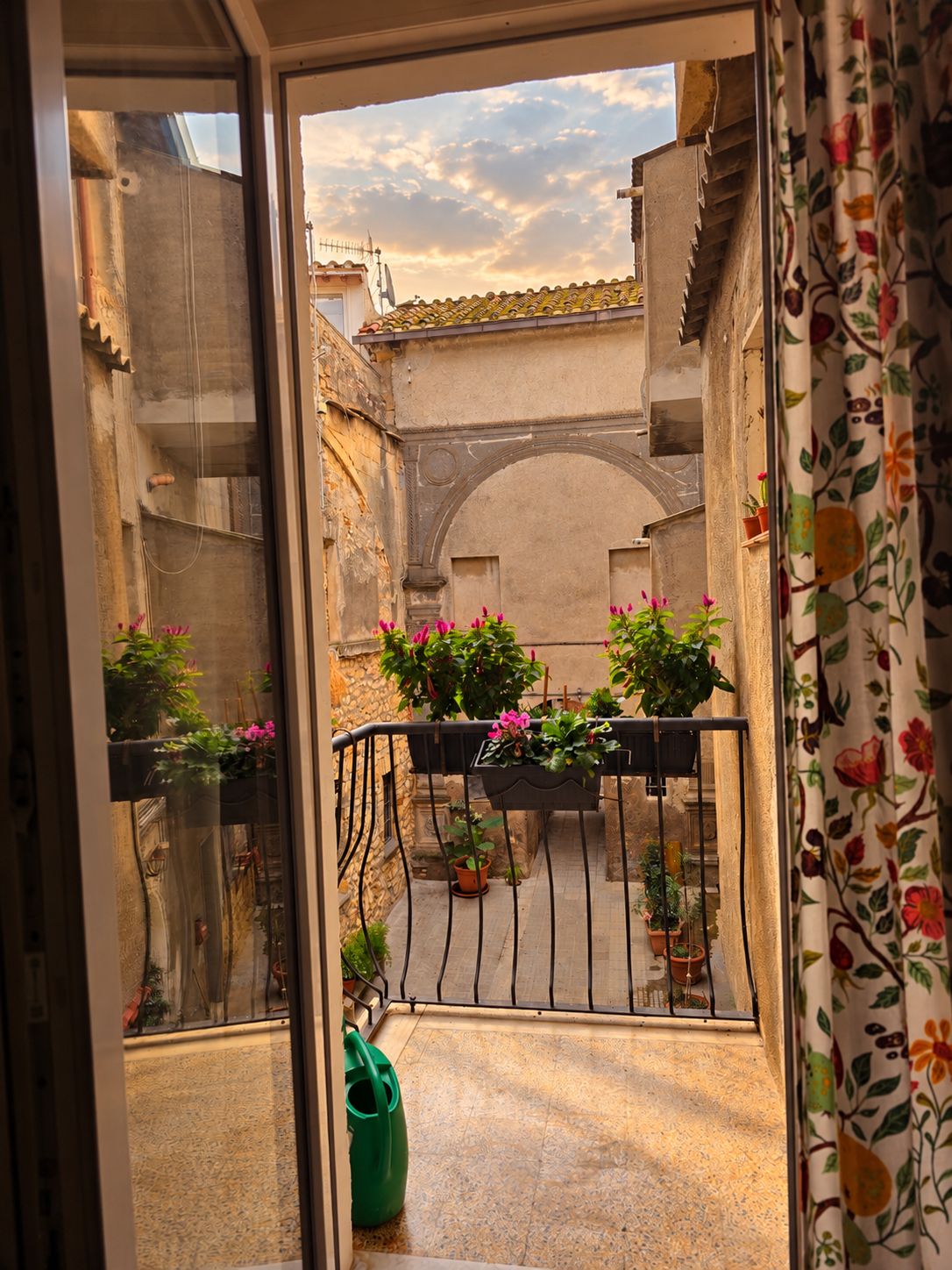 A balcony with potted plants and a view of a narrow street.