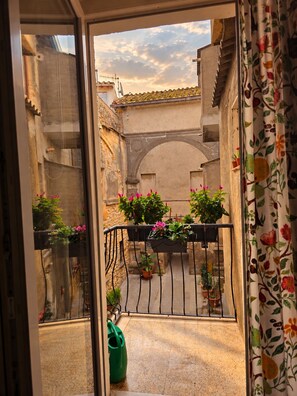 A balcony with potted plants and a view of a narrow street.