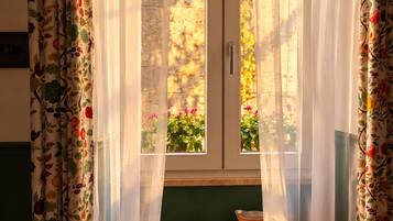 A room with a window covered by sheer curtains, a bowl, and an open book on a wooden surface.