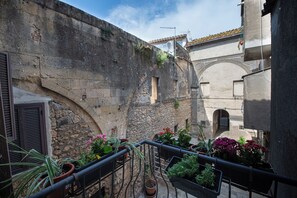 Un cortile stretto con pareti in pietra, una ringhiera metallica e piante in vaso.