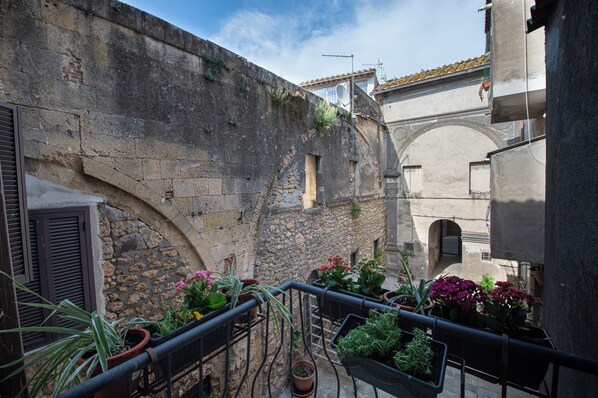 A narrow courtyard with stone walls, a metal railing, and potted plants.