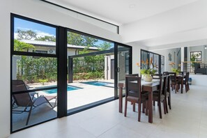 Ein moderner Essbereich mit Blick auf einen Pool, großen Schiebeglastüren und einer Küche im Hintergrund.