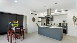 A modern kitchen with a central island, a dining area with wooden chairs, and a large window. - Side by Side Villas Walking Distance to Both Playa Tamarindo & Playa Langosta (Playa Langosta)