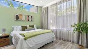 A bedroom with a bed, a nightstand, a lamp, a window with curtains, and a plant. - Side by Side Villas Walking Distance to Both Playa Tamarindo & Playa Langosta (Playa Langosta)