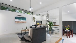 A modern living room with a grey sofa, a coffee table, and a TV mounted on the wall. There is a dining area with a wooden table and chairs. - Side by Side Villas Walking Distance to Both Playa Tamarindo & Playa Langosta (Playa Langosta)
