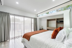 Ein modernes Hotelzimmer mit einem großen Bett, einem Nachttisch, einem fest installierten Fernseher und einem Fenster mit Vorhängen.