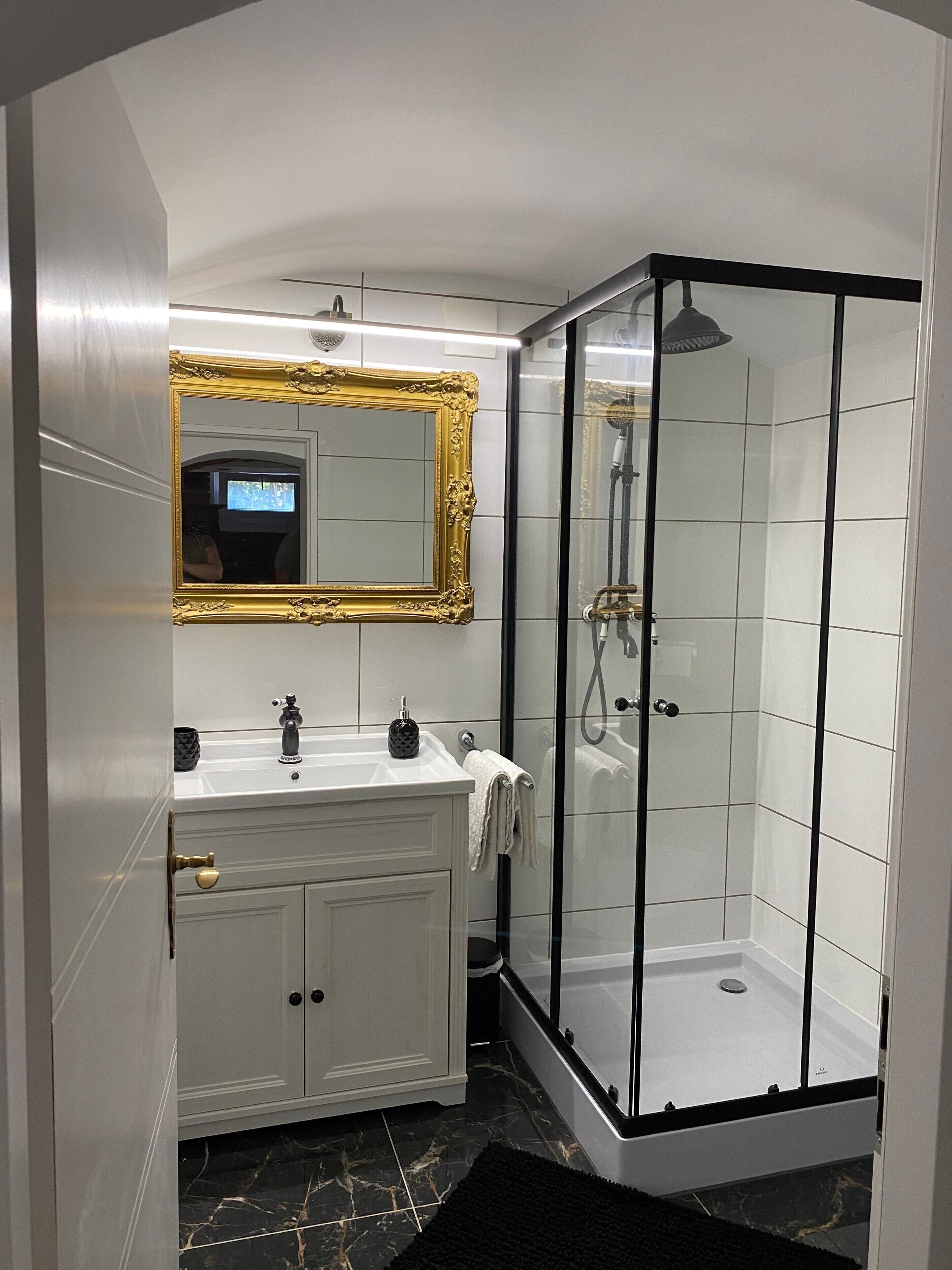 Een badkamer met een witte wastafel, een spiegel met gouden lijst, een douchecabine van glas en een marmeren vloer.