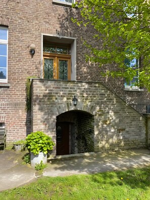 Ein Backsteinhaus mit steinernen Torbogen, einem Fenster mit Metallgitter und einem kleinen Gartenbereich mit einem Blumentopf.