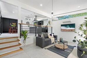 Ein modernes Wohnzimmer mit einem grauen Sofa, einem Couchtisch und einem Fernseher. Eine Treppe mit Holzbodenstufen führt zu einer weiteren Ebene.